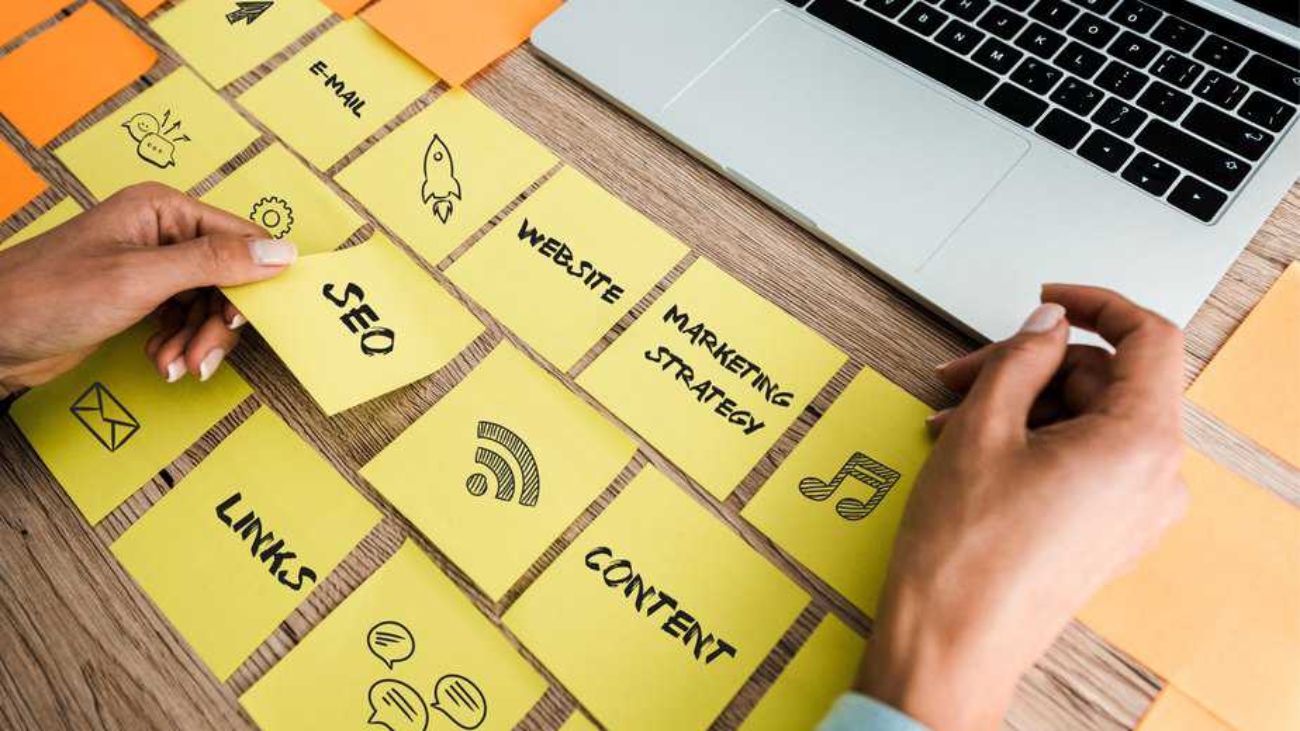 cropped view of woman touching sticky note with seo lettering near laptop on desk