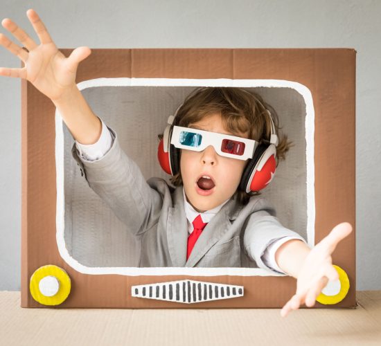 Child playing with cardboard box TV. Kid having fun at home. Video blogging concept