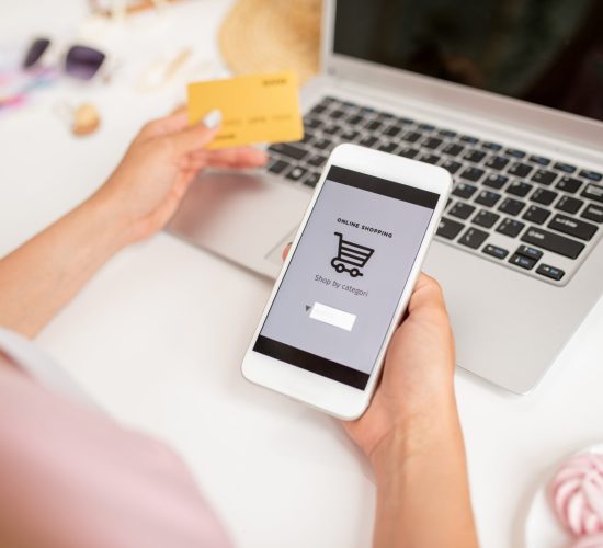 Smartphone held by young contemporary mobile shopper searching for goods to add new ones in basket